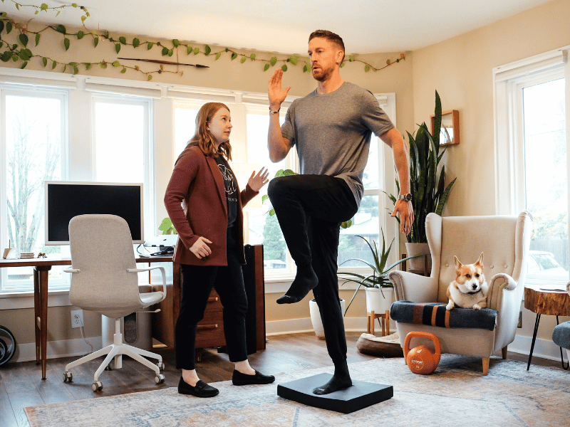 A MovementX physical therapist helping a patient do balance exercises in their home on a balance pad.