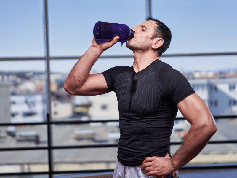 A man drinking water at the end of a physical therapy routine outdoors.