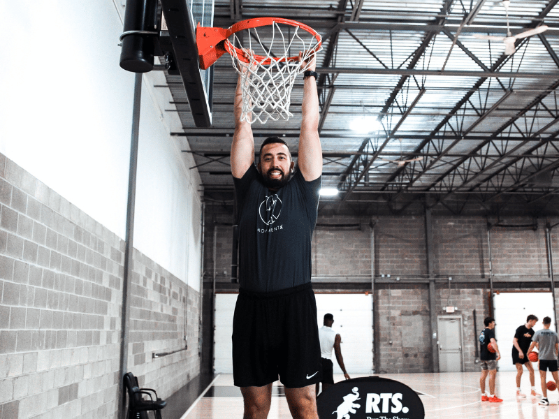 Patrick Dumais, PT, DPT hanging from the rim of a basketball hoop.