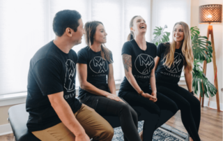 a group of 4 movementx physical therapists sitting on a treatment table in a home setting wearing shirts with the logo of their PT job