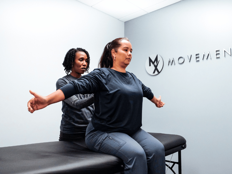 Dr. Suzanne Cowan helping a patient go through a shoulder and back mobility assessment on a PT table in a MovementX location.