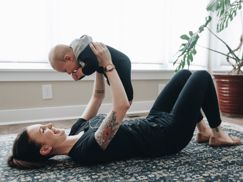 A mother playing with her baby on the floor of her living room.