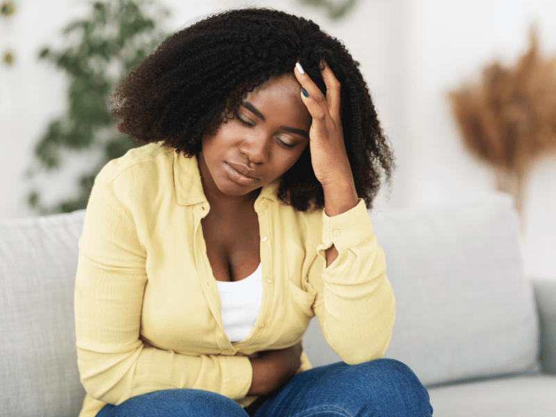 A woman with her hand on her bladder in pain, sitting on a couch.