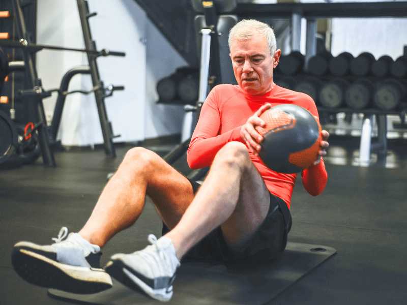 Our fictional patient, John, doing russian twists with a medicine ball in his 60s.