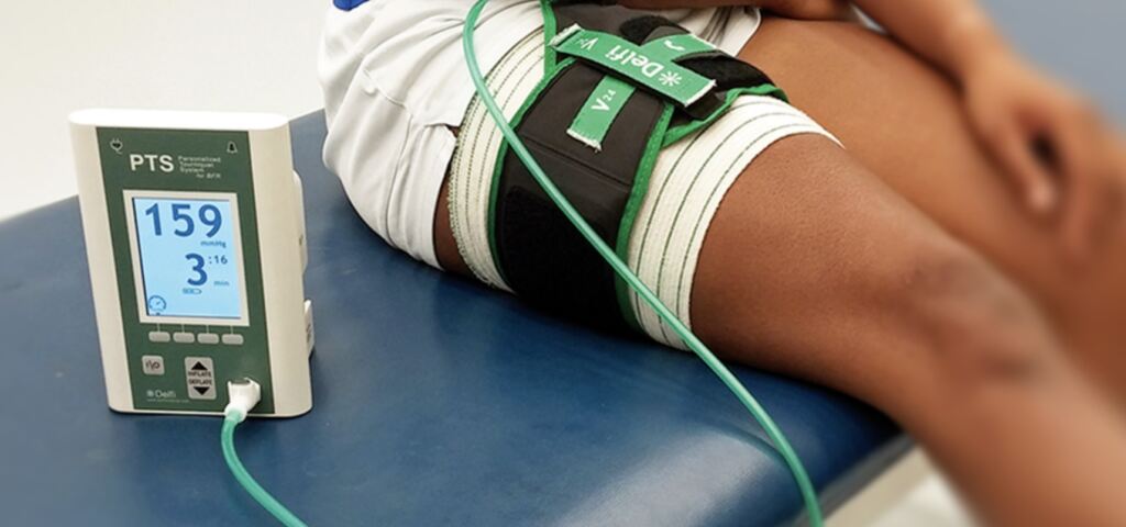 A Blood Flow Restriction cuff on a person's leg, next to an occlusion machine.