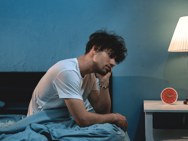 A man sitting on the edge of his bed wondering how to get better sleep.