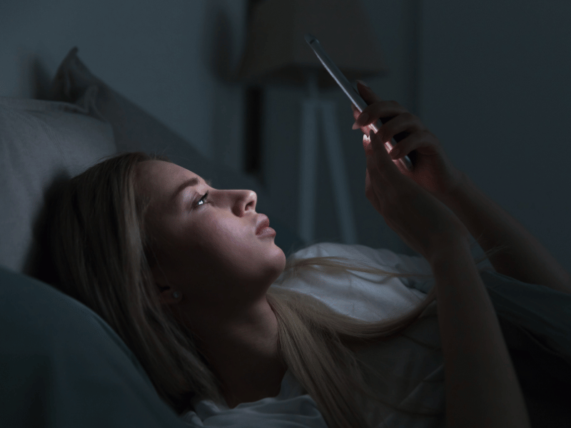 A woman laying in bed with her phone, illuminated by the blue light of her screen.