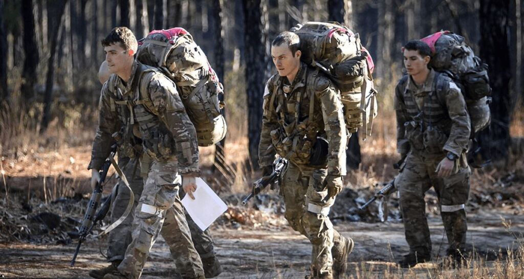 A group of soldiers marching with heavy weighted packs on their backs.