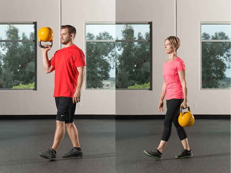 A man and a woman doing varied kettlebell carries.