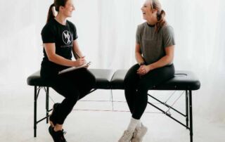 a movementx physical therapist consulting with a new patient in a home while sitting on a treatment table