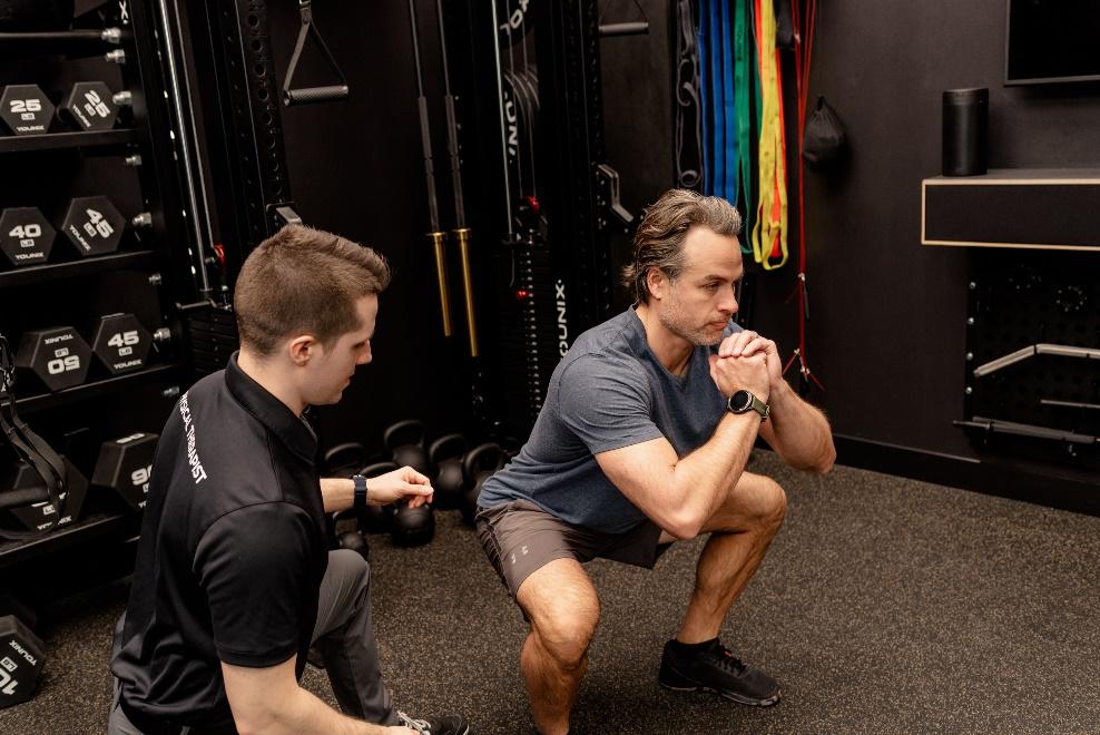 Adam Kays helping a patient through a squat and low-back pain series of exercises.
