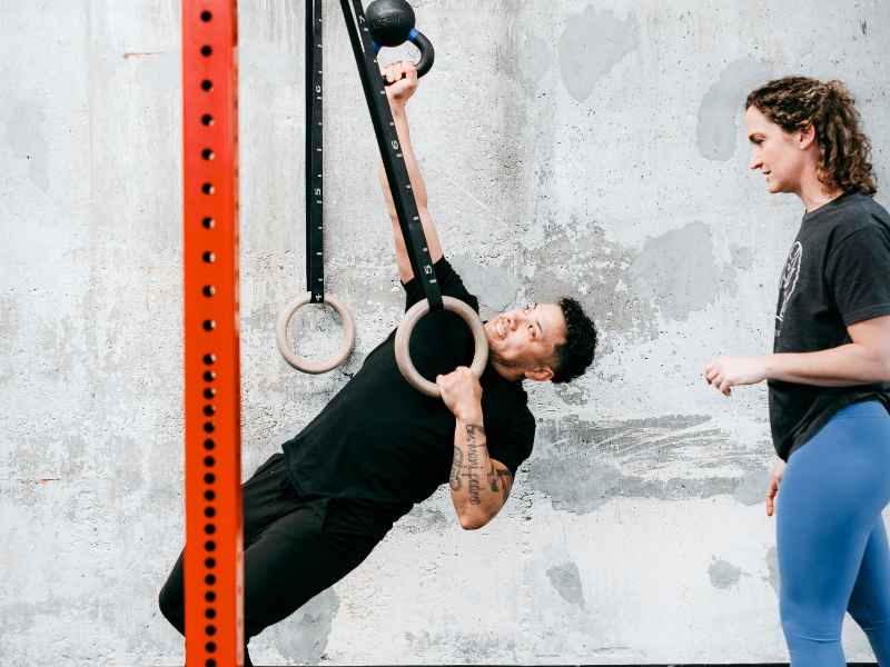 Kristen Lattimore, PT, DPT helping a patient strengthen and address thoracic rotation in a gym using gymnast rings and a kettlebell.