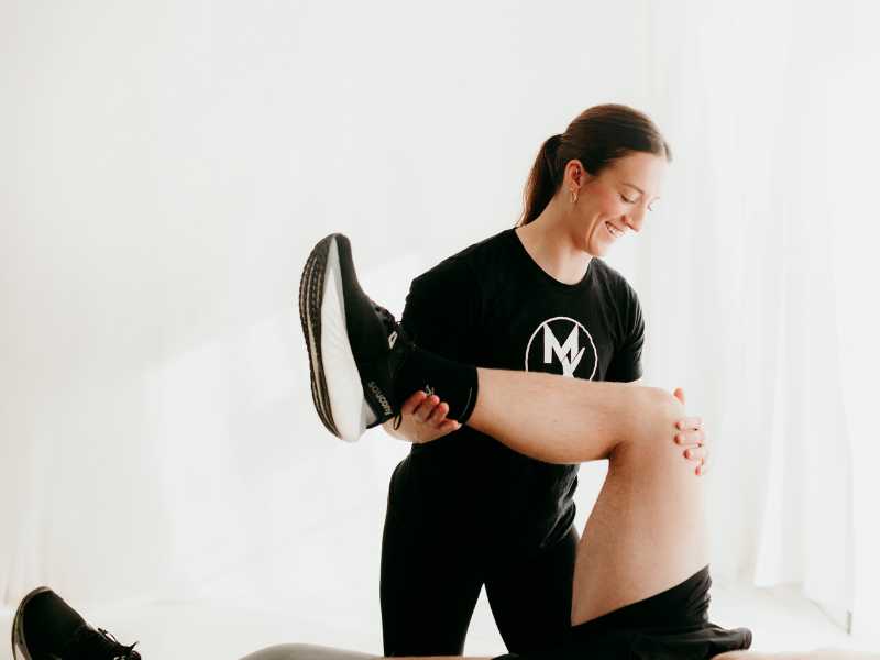 A MovementX physical therapist working with a runner on a treatment table, taking them through a series of mobility tests with their left leg.