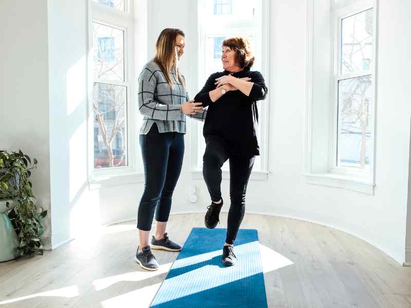 A MovementX physical therapist helping an older patient practice balance exercises in their own home during a session.