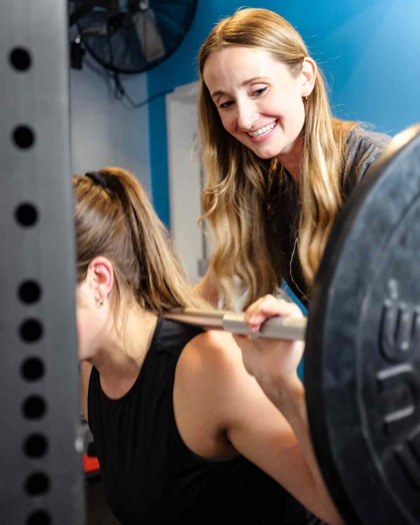 A MovementX provider helping a patient do pain-free back squats in a power rack.