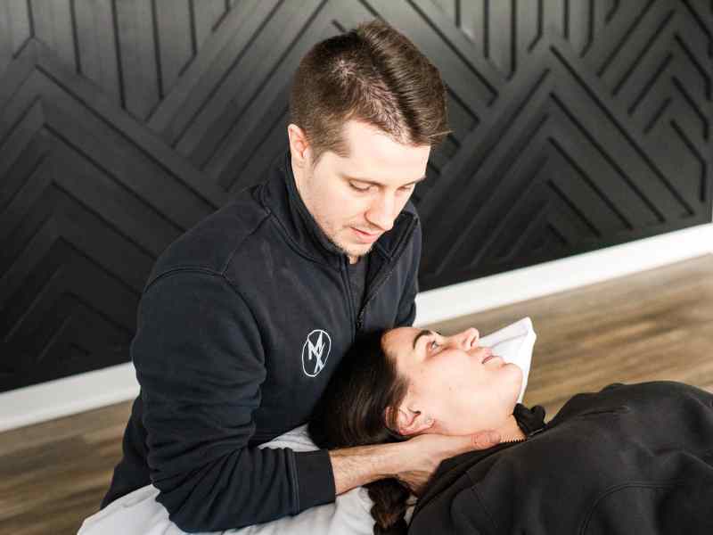 Adam Kays, PT, DPT with MovementX helping a patient stretch her neck during a session in home.