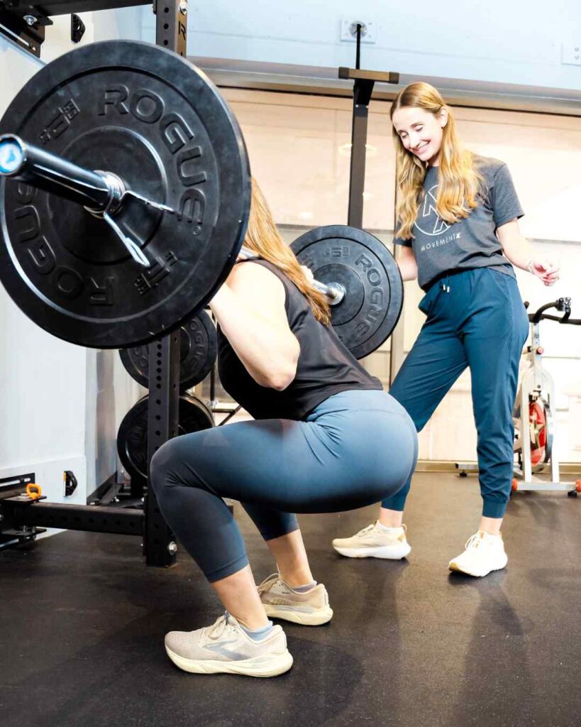 Natalie de Selding, PT, DPT helping a patient adjust her back squat technique during a physical therapy sessions.