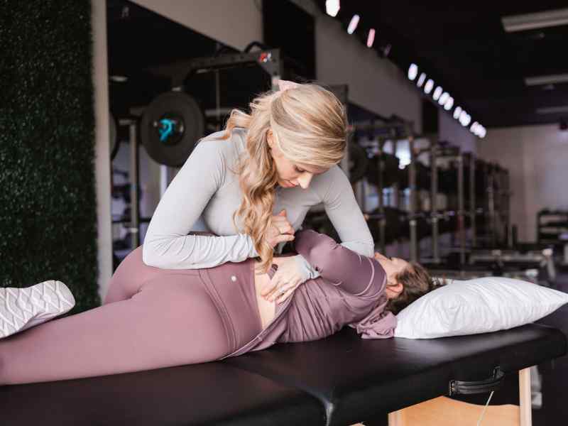 A MovementX provider helping a female patient do a lower back adjustment during a treatment session.