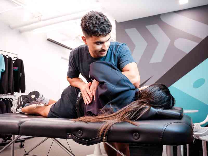 MovementX provider Cesar Laboy, PT, DPT helping a patient release their lower spinal tension on a treatment table in a gym.