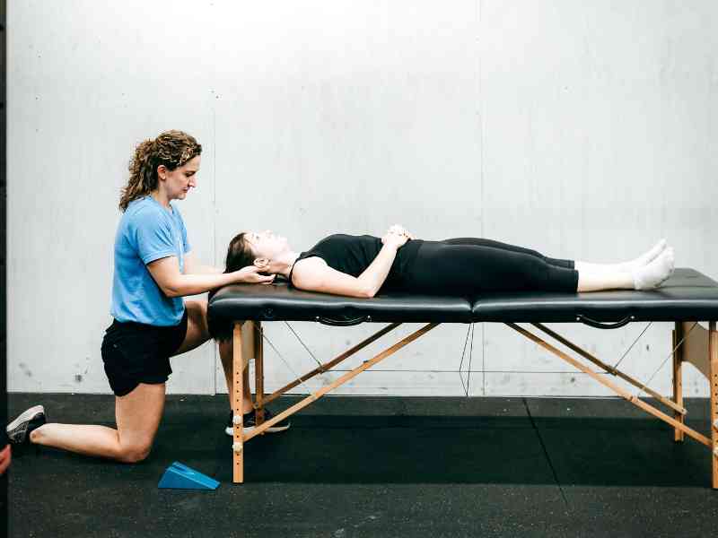 MovementX provider Kristen Lattimore, PT, DPT helping a patient on a treatment table adjust and assess her neck mobility.