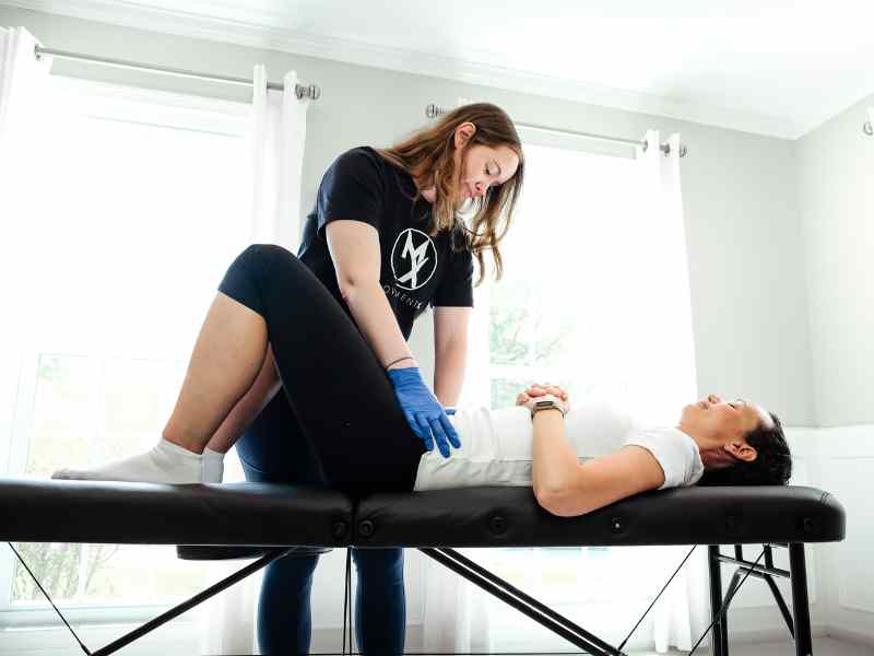 MovementX physical therapist Morgan Groover helping a patient on a treatment table in their home.