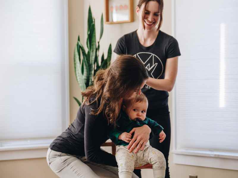 A MovementX provider helping a new mother work through basic movements while carrying her baby, in her home.