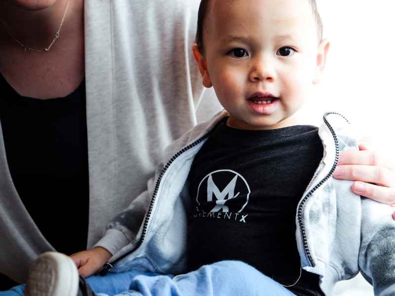 A toddler wearing a MovementX t-shirt while sitting on their mothers lap.