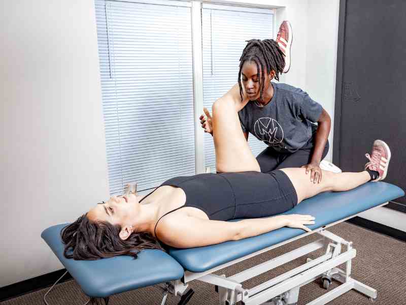 MovementX Doctor of Physical Therapy, Bridget Ochuko, helping a female patient stretch and open up her hip and pelvic region during a physical therapy session in Durham, North Carolina.