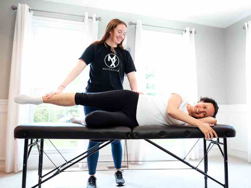 MovementX provider Morgan Groover, PT, DPT helping a patient test her hip mobility on a treatment table in-home.