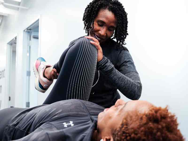 MovementX Provider Suzanne Cowan helping a female patient test knee flexion on a treatment table.