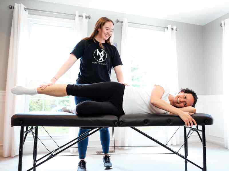 MovementX Provider Morgan Groover helping a patient test knee and hip mobility on a treatment table during an in home session.