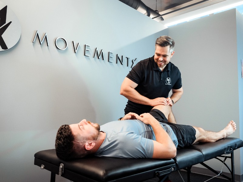 A MovementX provider helping a patient with knee pain on a treatment table.