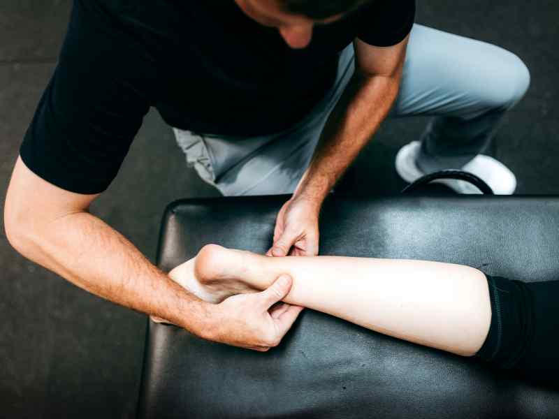 A MovementX provider performing manual therapy on a patient's achilles tendon on a treatment table.