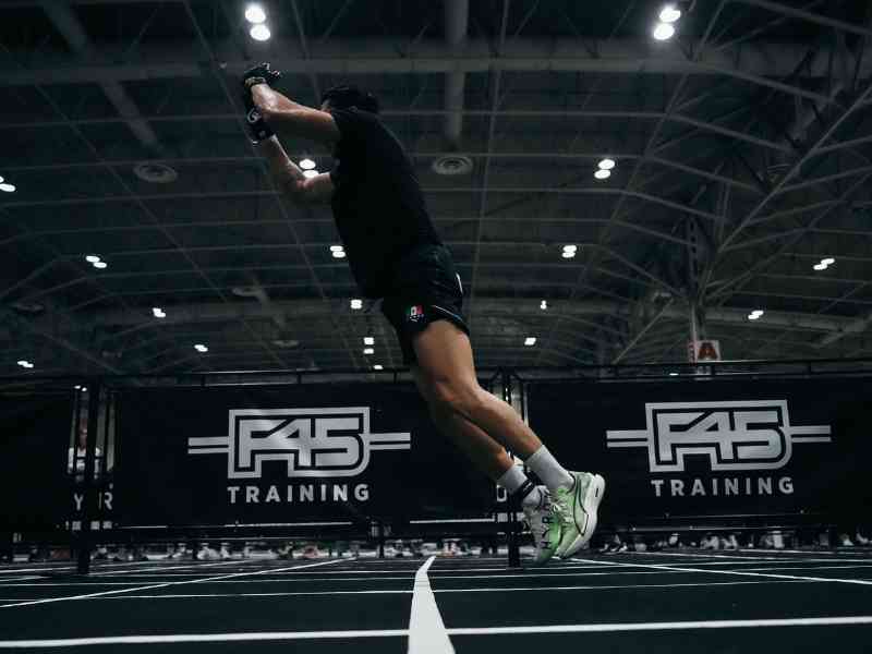 An endurance athlete doing a lateral jump during a functional fitness event indoors on turf.