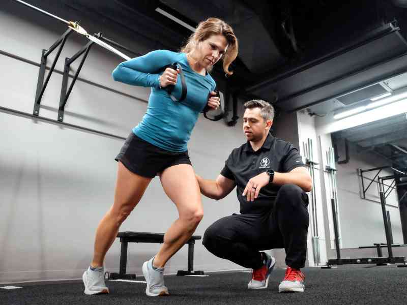 James Cousler, PT, DPT helping a patient perform stronger TRX rows during a physical therapy session in a gym.