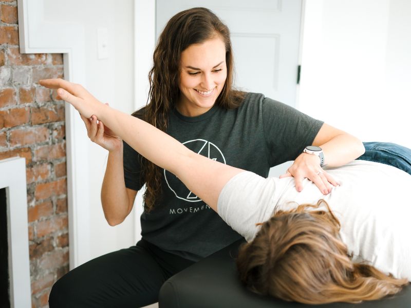 MovementX Provider Ashton Grimm, PT, DPT helping a patient mobilize her shoulder on a treatment table.