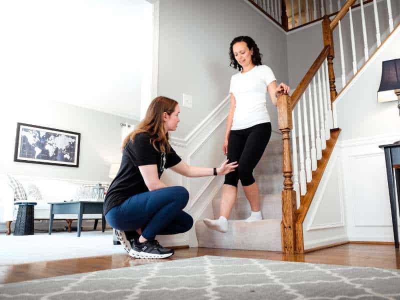 Morgan Groover, PT, DPT helping a patient do calf raises on a staircase in home during a physical therapy session.
