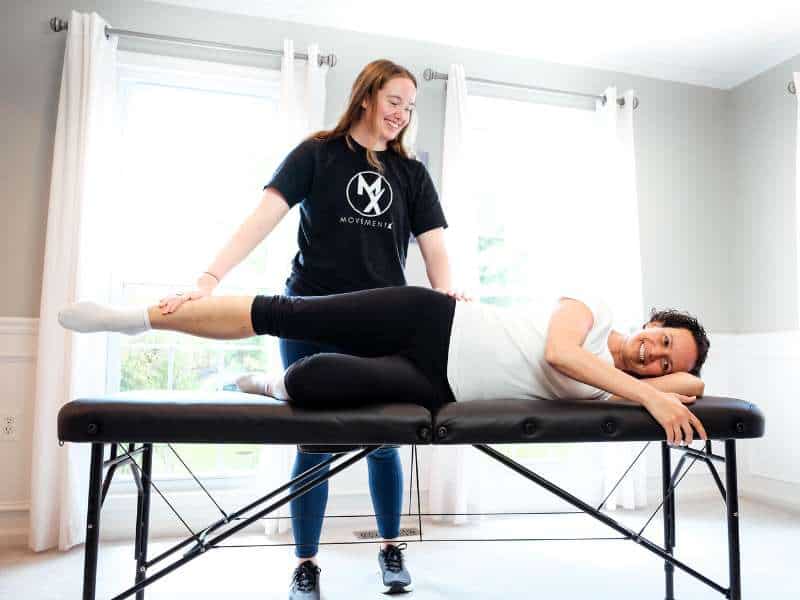 Morgan Groover, PT, DPT guiding a patient through mobility exercises on a treatment table in home.