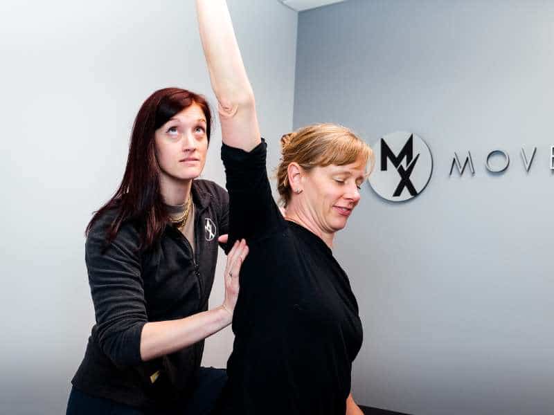 MovementX provider Colleen Gallagher, PT, DPT assessing a patient's shoulder mobility on a treatment table in Northern Virginia.