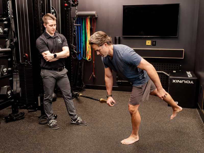 MovementX Provider Adam Kays, PT, DPT helping an older patient do a balance exercise in a gym treatment session.