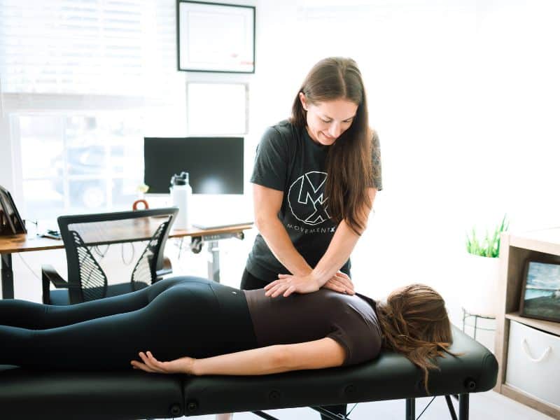 A MovementX provider helping a patient feel and manipulate their intercostal muscles on a treatment table in their home.