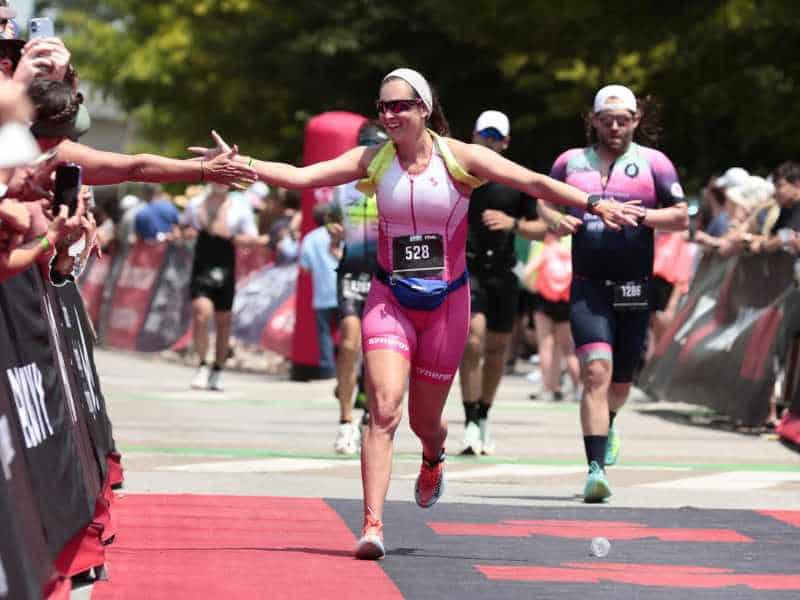 MovementX Provider Ashton Grimm, PT, DPT running near the finish line to an Ironman race while high fiving a spectator.