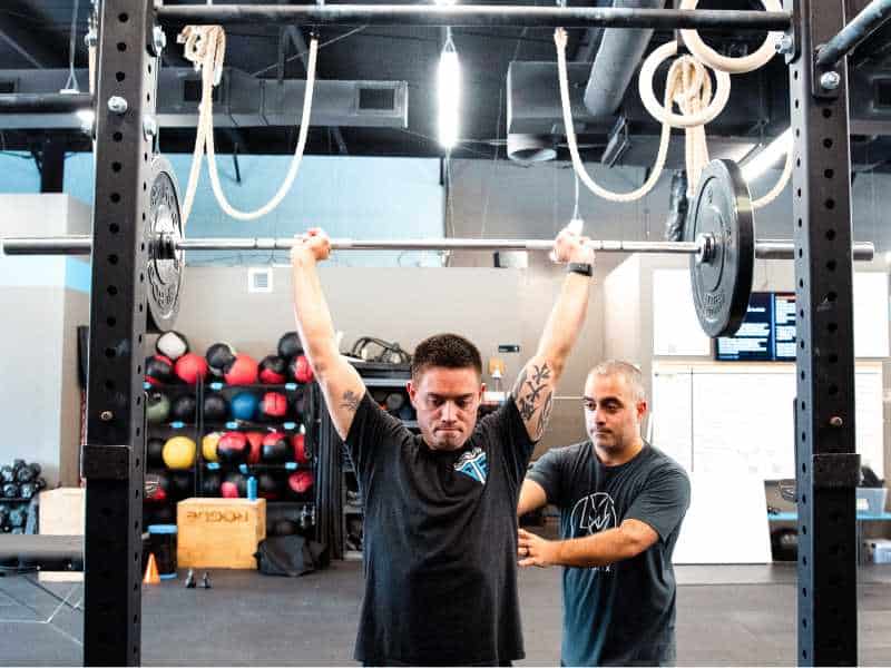 MovementX provider, Romin Ghassemi, PT, DPT, helping a patient perform an overhead lift in a CrossFit gym