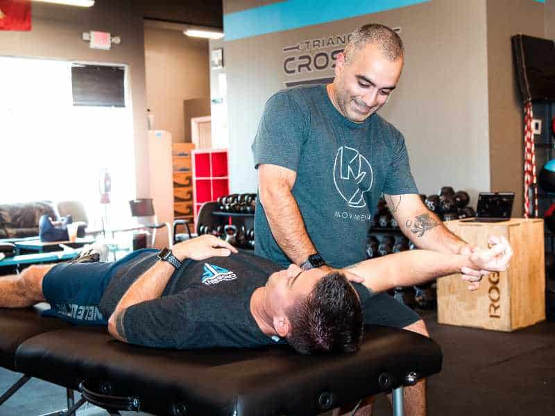 MovementX provider, Romin Ghassemi, PT, DPT, helping a patient mobilize their shoulder on a treatment table in North Carolina