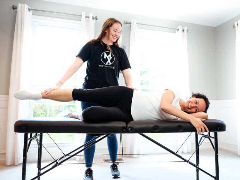MovementX Provider Morgan Groover, PT, DPT helping a patient test her leg mobility on a treatment table in-home.