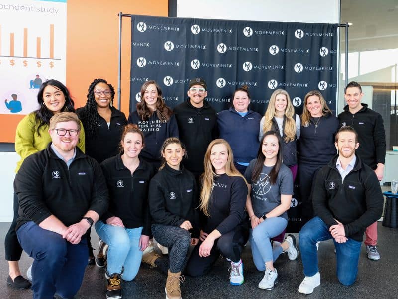 The MovementX NOVA/DMV team stood together for a group photo in front of a MovementX backdrop, all smiling.