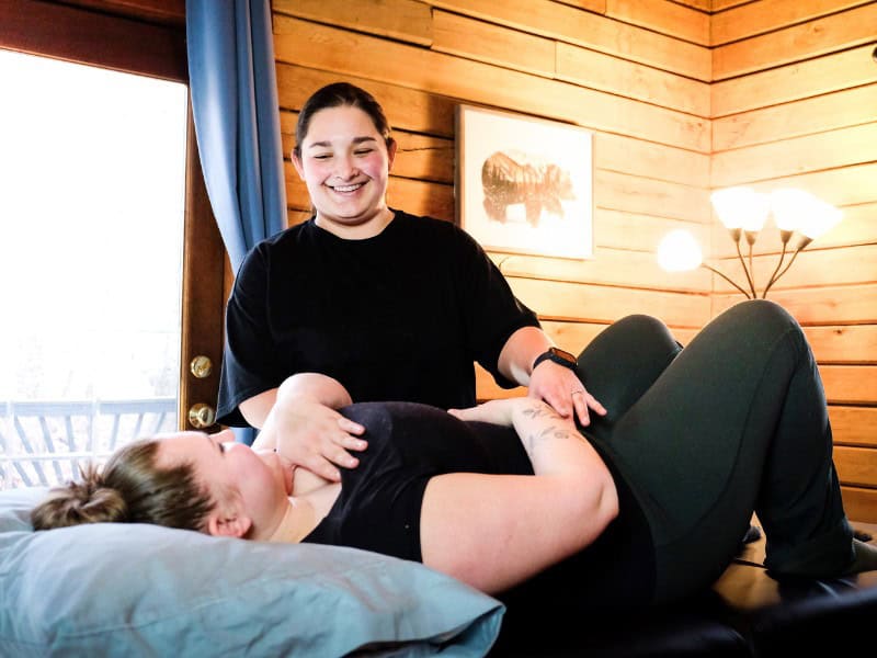 A MovementX Provider discussing pelvic health needs with her patient while the patient lays on a treatment table in a home setting.