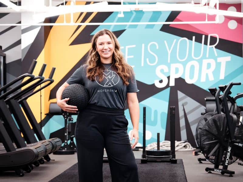 MovementX provider Michelle Bomyea, PT, DPT standing holding a medicine ball in a gym's functional training area.