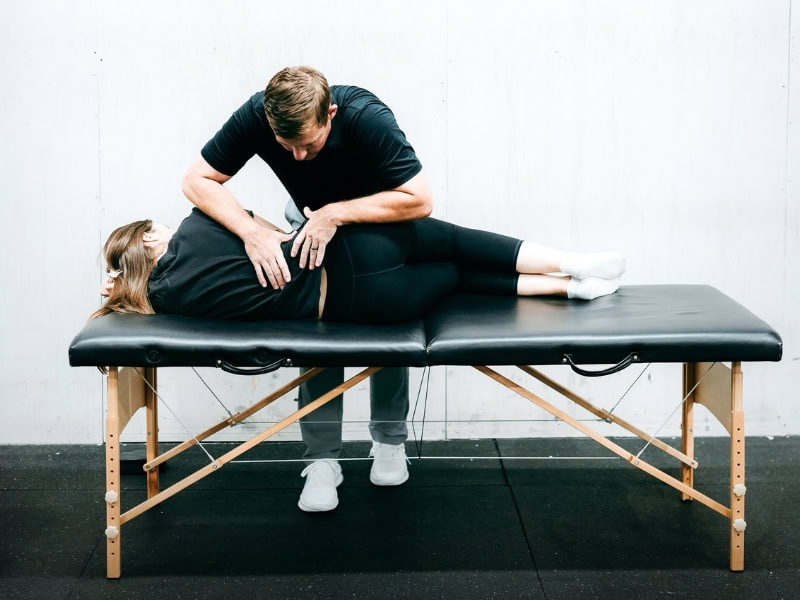 MovementX provider Tyler Eubanks helping a patient release lower back pain on a treatment table.